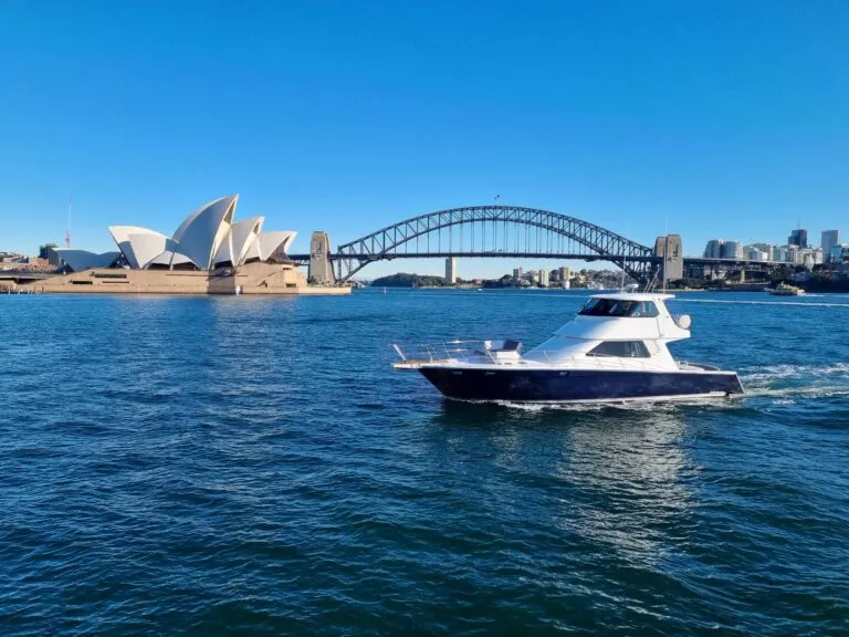 Side profile of State of the Art yacht cruising past Sydney Harbour Bridge