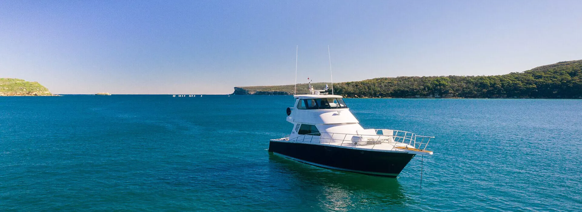 State of the Art yacht anchored on calm blue waters near a forested Australian coastline under a clear sky