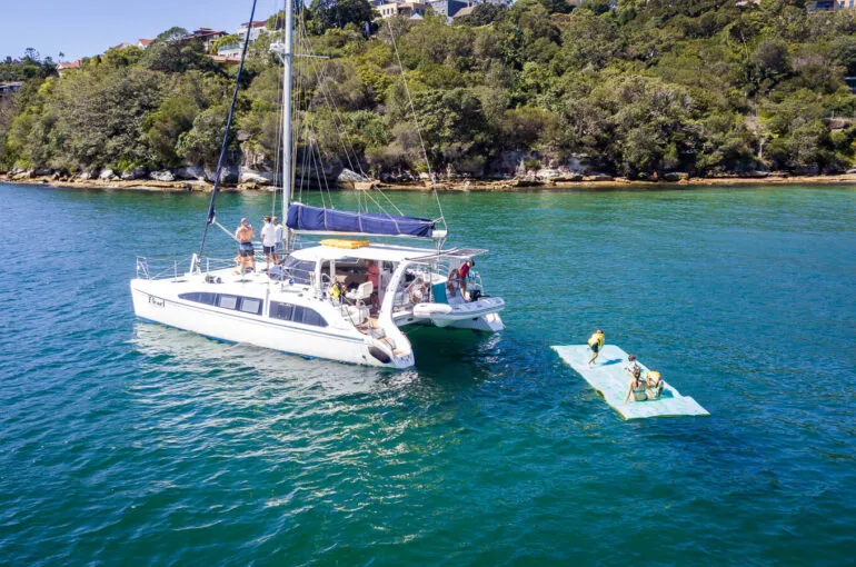Pearl Catamaran anchored near a green shoreline with people on a raft.