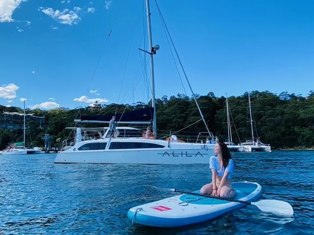 A woman sits on a paddleboard near the Alila yacht in clear water.