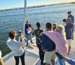 Group gathered on a spellbound boat, enjoying a sunny day by the water.