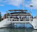 White catamaran named Spellbound docked in calm waters under a blue sky.