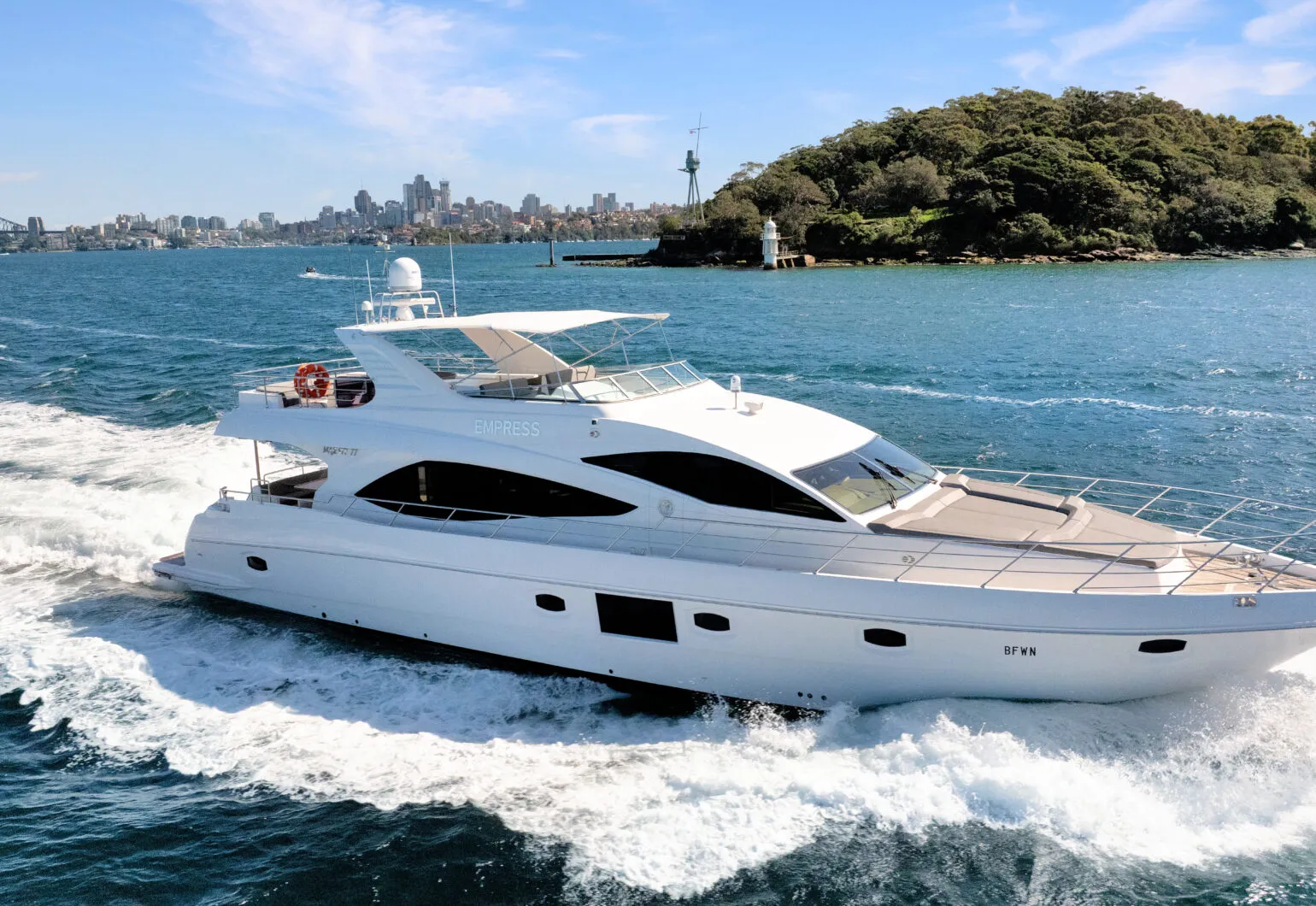 Empress motoryacht cruising near Sydney headland with lighthouse and city skyline in the background – Dreamboats