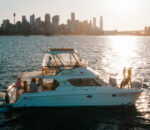 Life’s Good catamaran sailing near a city skyline at sunset. Variation #1: Life’s Good catamaran anchored with city skyline glowing in the background.