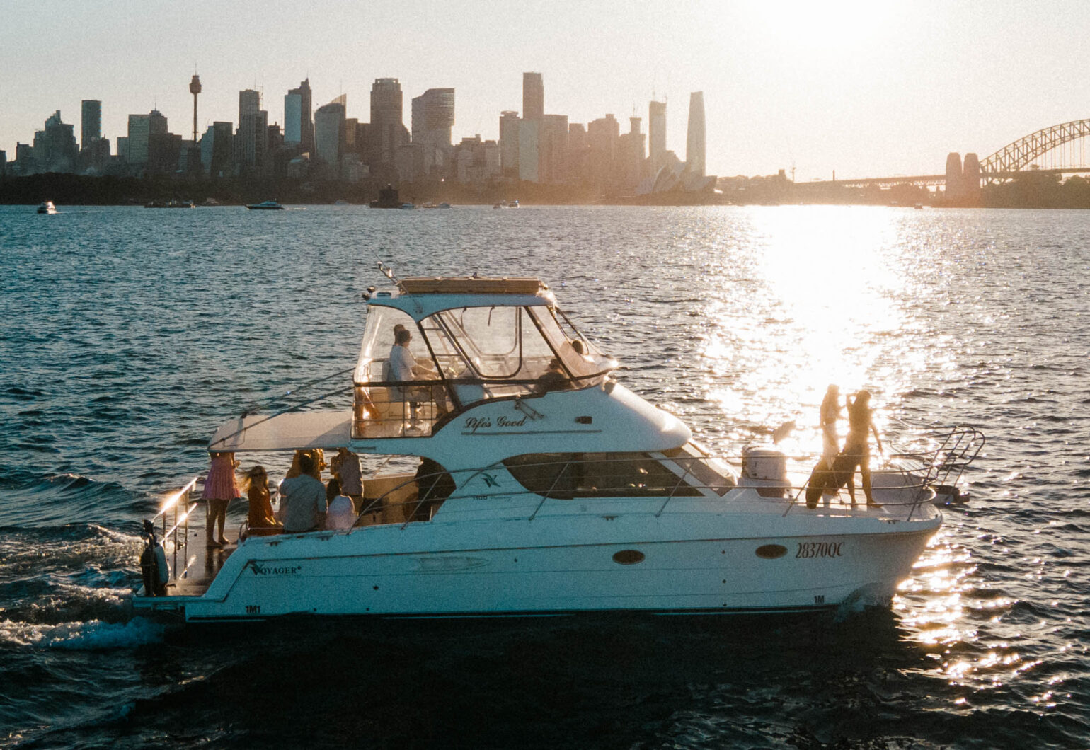 Life’s Good catamaran sailing near a city skyline at sunset. Variation #1: Life’s Good catamaran anchored with city skyline glowing in the background.