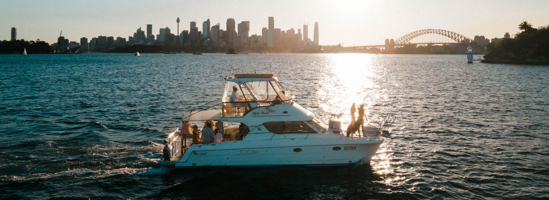 Life’s Good catamaran sailing near a city skyline at sunset. Variation #1: Life’s Good catamaran anchored with city skyline glowing in the background.