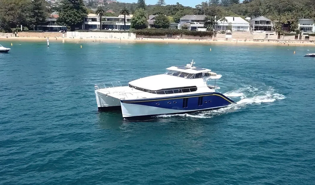 Sleek Passion Catamaran cruising on clear blue water near a sandy beach. Variation #1: Modern Passion Catamaran gliding through turquoise waters by the shore.